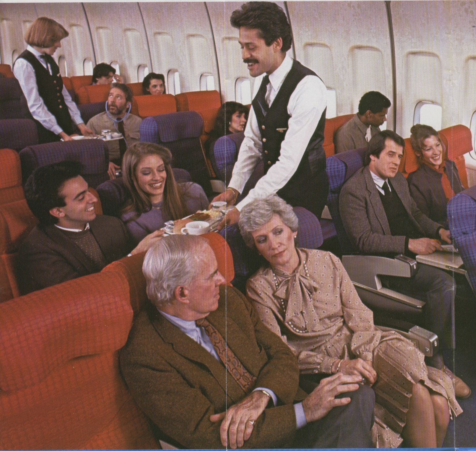1980s The economy section of a Pan Am 747 during meal service.  The male flight attendant is Carlos Rosalino.